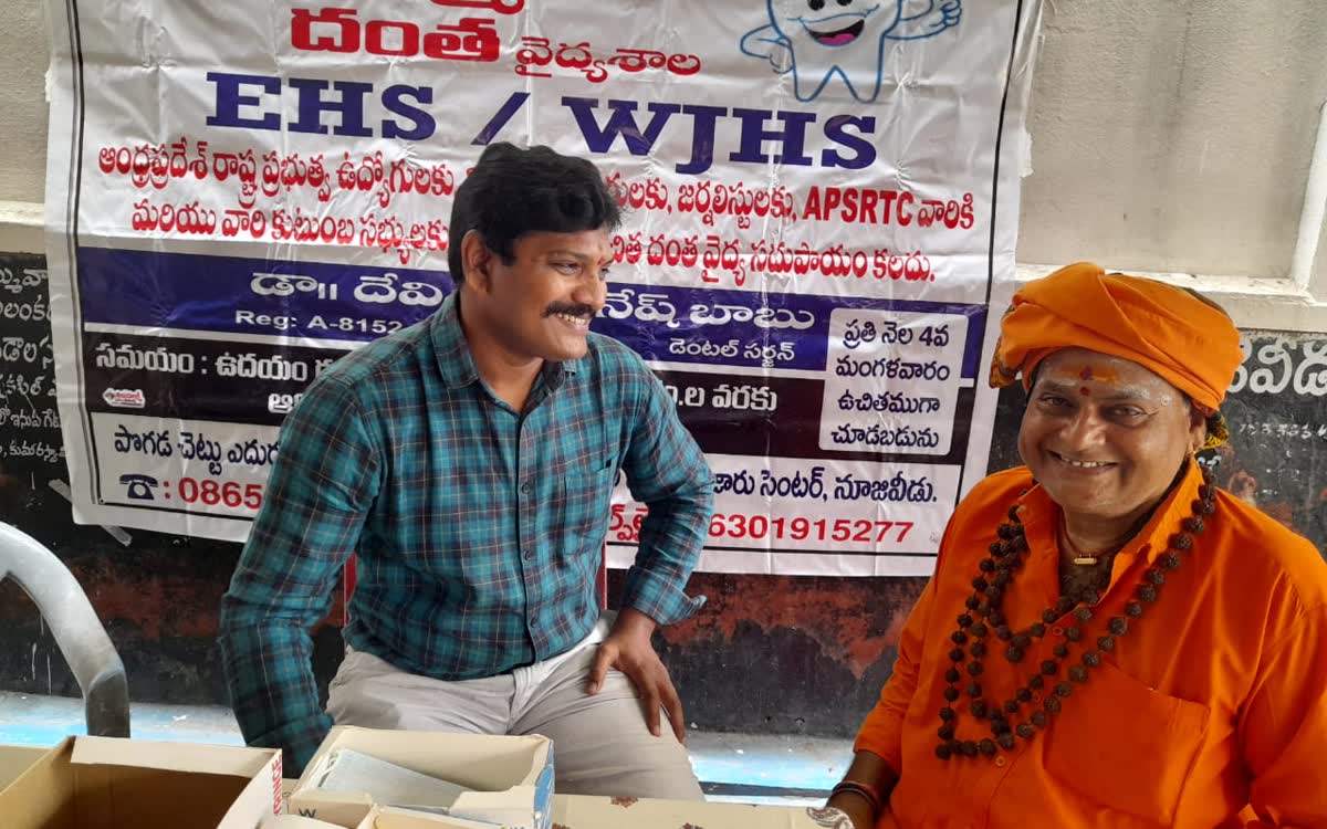 Guruji seated with the visiting dentist beneath the dental clinic banner