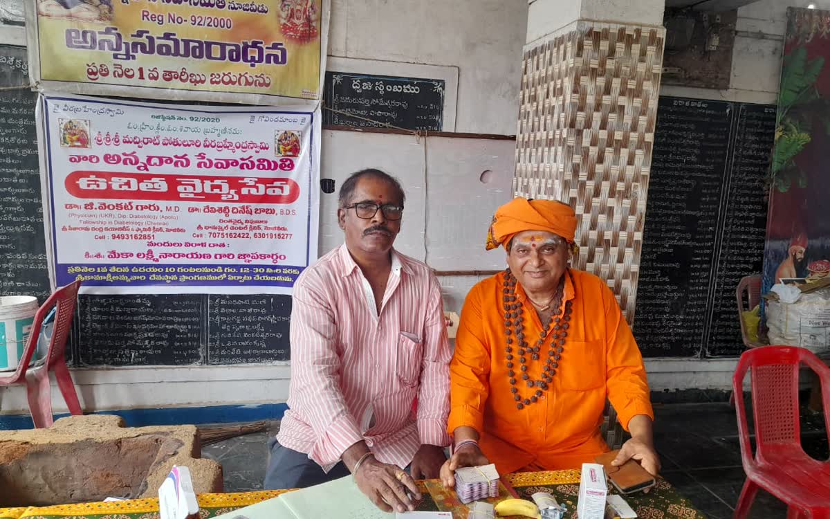 Guruji seated beside a table of medicines under the camp banner