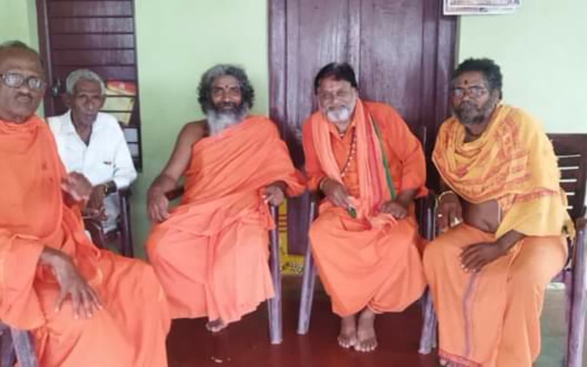 Four sadhus in ochre robes seated together on chairs at the Samithi