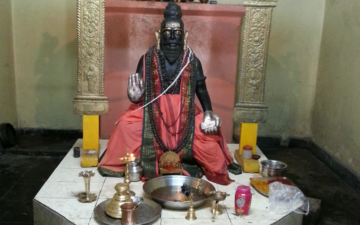 The Swamy&rsquo;s idol seated under a silver arch, lamps and offerings before it